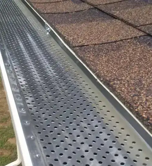 Perforated gutter guard installed along a shingled roof edge