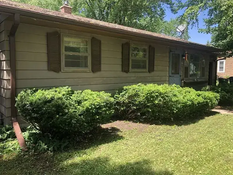 Tan ranch house with shutters and shrubs along the front