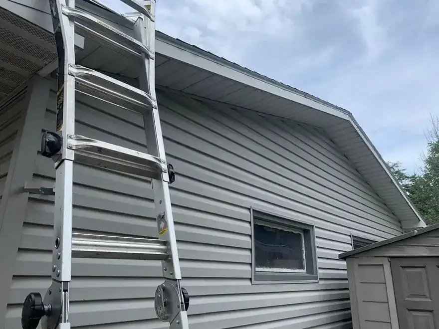 Ladder leaning against gray siding at the eave